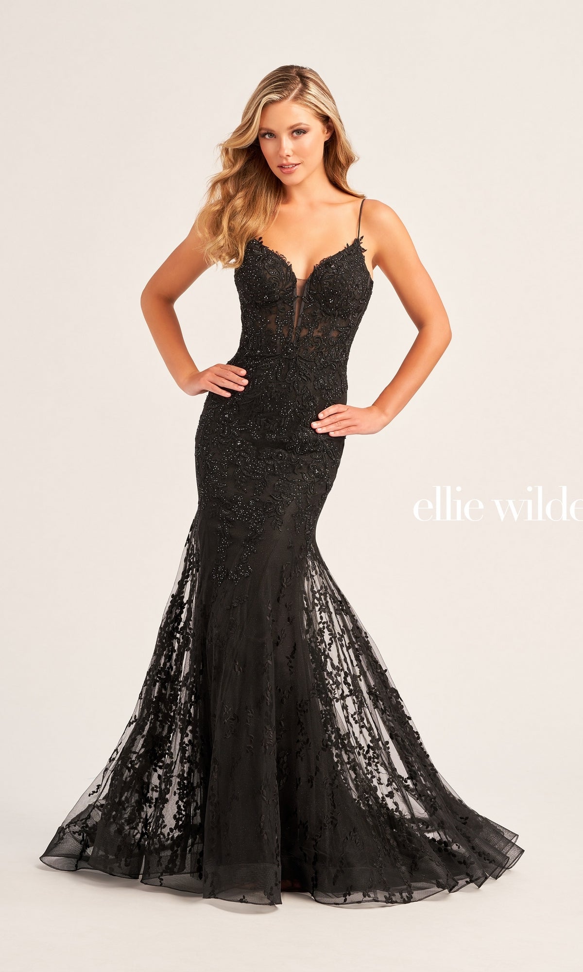 A woman poses in the Ellie Wilde Beaded-Tulle Long Prom Dress EW35010, a fitted black mermaid gown with beaded embroidery and spaghetti straps, sheer bodice detail, standing against a plain light background.